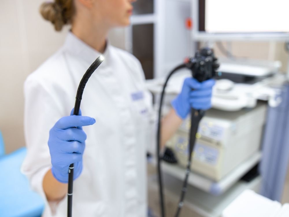 Médica segurando endoscópio com ponta iluminada em ambiente hospitalar, reforçando a segurança e os mínimos riscos da endoscopia.