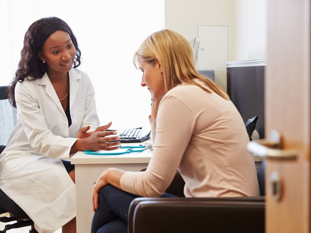 Mulher em consulta médica com gastroenterologista investigando sintomas como fezes finas e dores abdominais.