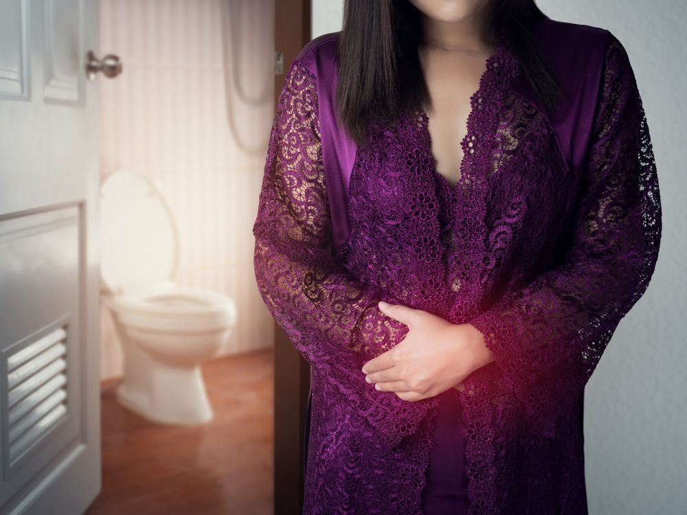 Mulher com as mãos sobre o abdômen sentindo desconforto intestinal, sinal de possíveis fezes finas.