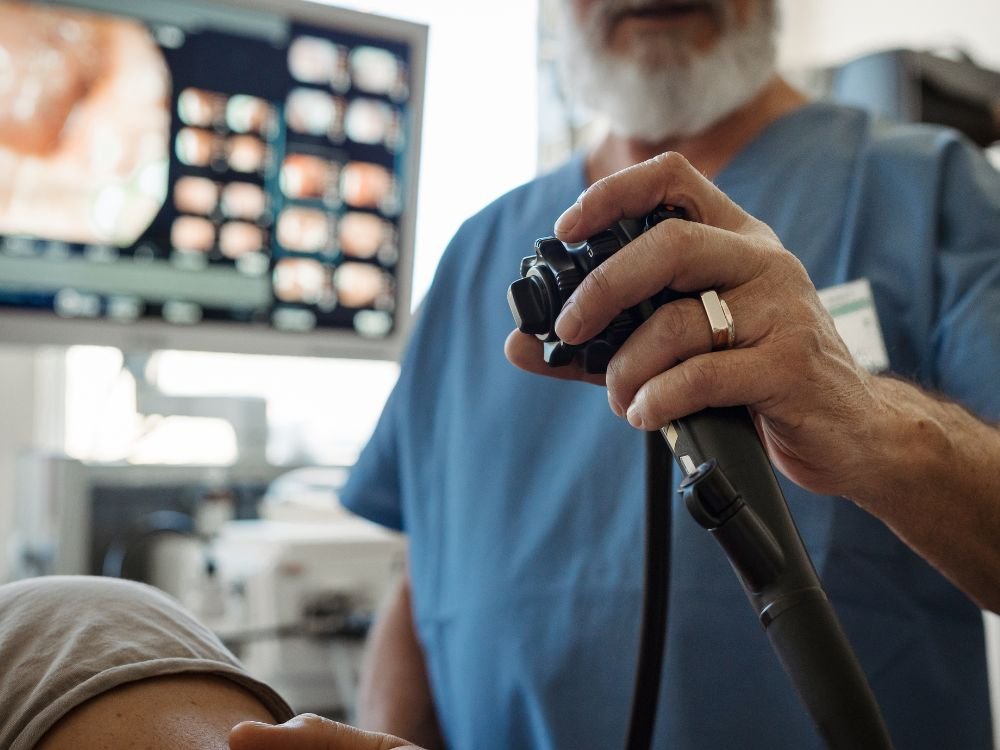 Médico ajustando o equipamento de colonoscopia durante o procedimento, exemplificando Como funciona a sedação para colonoscopia? para reduzir desconforto do paciente.