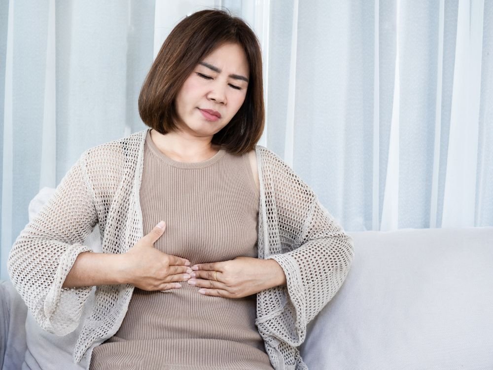 Mulher com dor abdominal segurando o estômago, situação comum em casos de estômago inflamado o que fazer diante dos sintomas