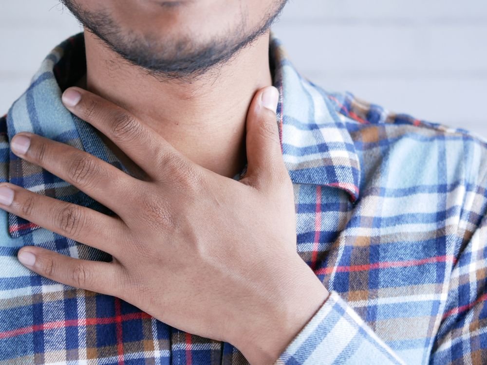 Homem com a mão na garganta representando dificuldade para engolir alimentos e desconforto ao engolir.