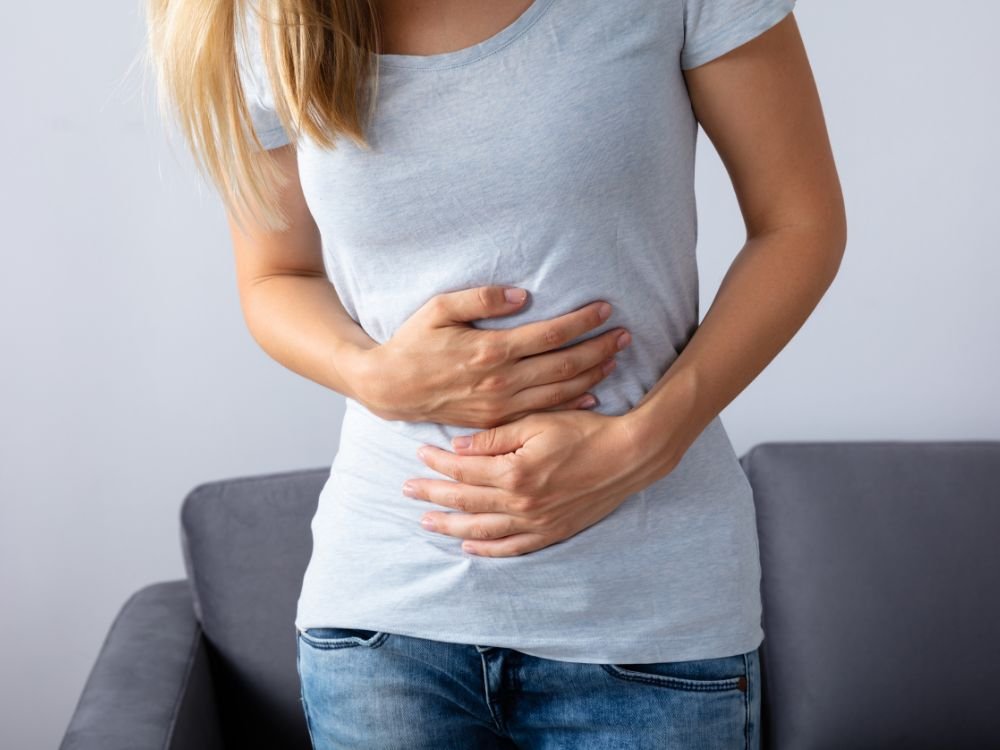Mulher com dores abdominais ilustrando sintomas de diarreia grave após uso de antibióticos causada por infecção intestinal recorrente.