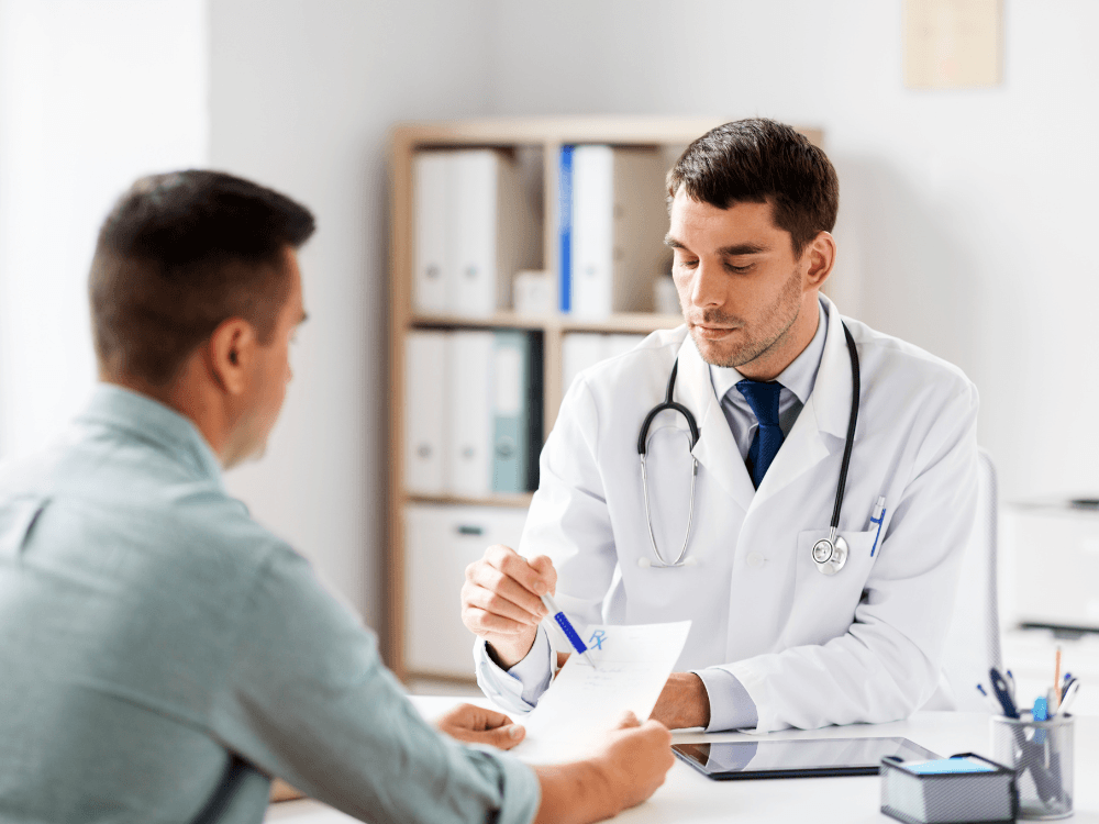 Médico entrega uma prescrição ao paciente durante consulta, explicando para ele, sobre refluxo o que é.