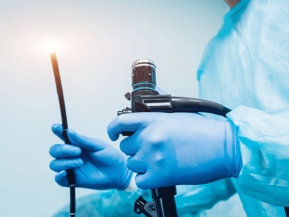 Profissional com luvas segura um aparelho de endoscopia usado na avaliação do sistema digestivo e coleta de biópsias.