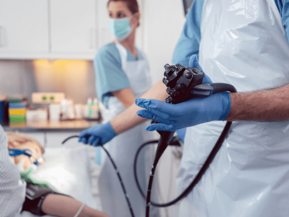 Equipe médica realiza uma endoscopia digestiva com aparelho inserido no paciente durante procedimento em ambiente hospitalar.