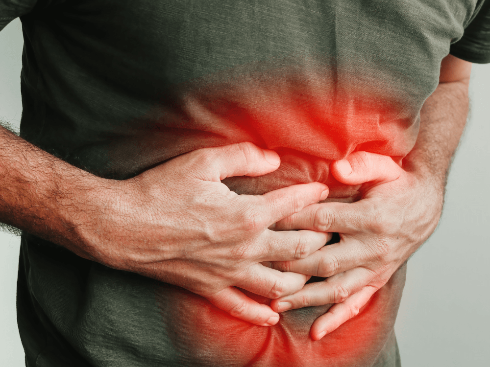 Pessoa com as mãos sobre a barriga e áreas avermelhadas, representando dor e desconforto abdominal entre os sinais de gastrite.