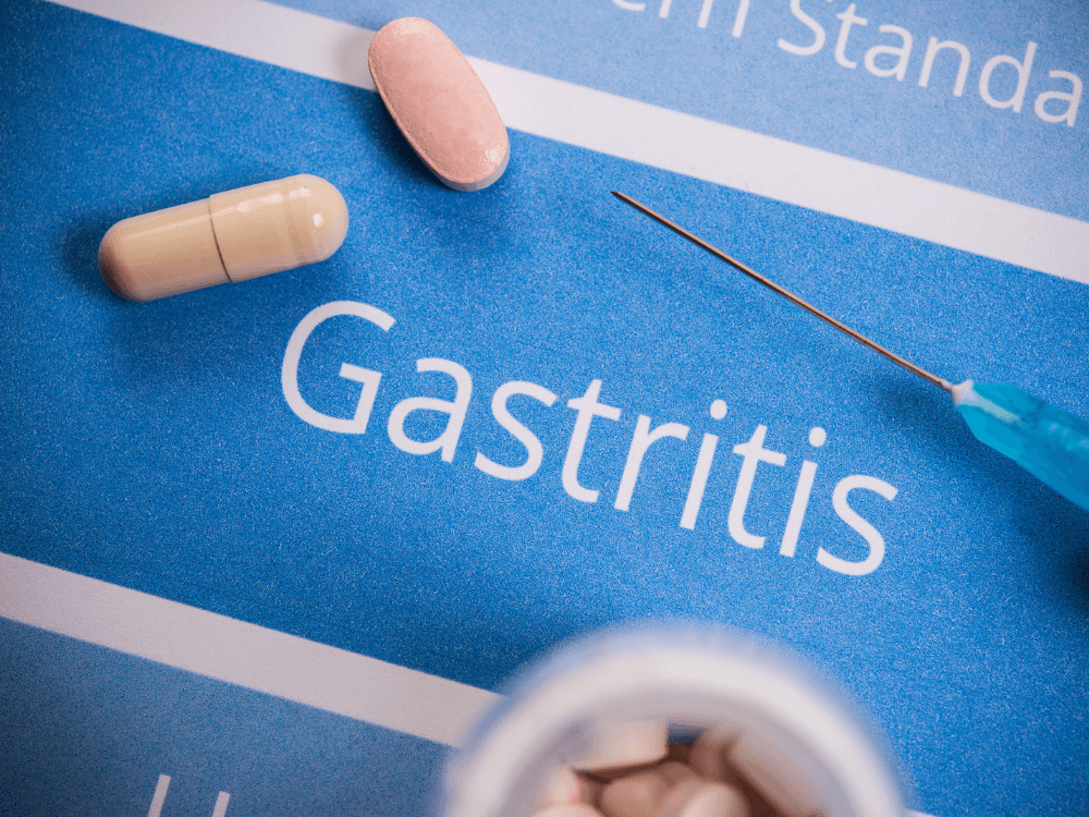 Medicamentos sobre material médico com a palavra gastrite em destaque, representando o tema da inflamação do estômago. Tudo para explicar como a gastrite ataca o organismo.